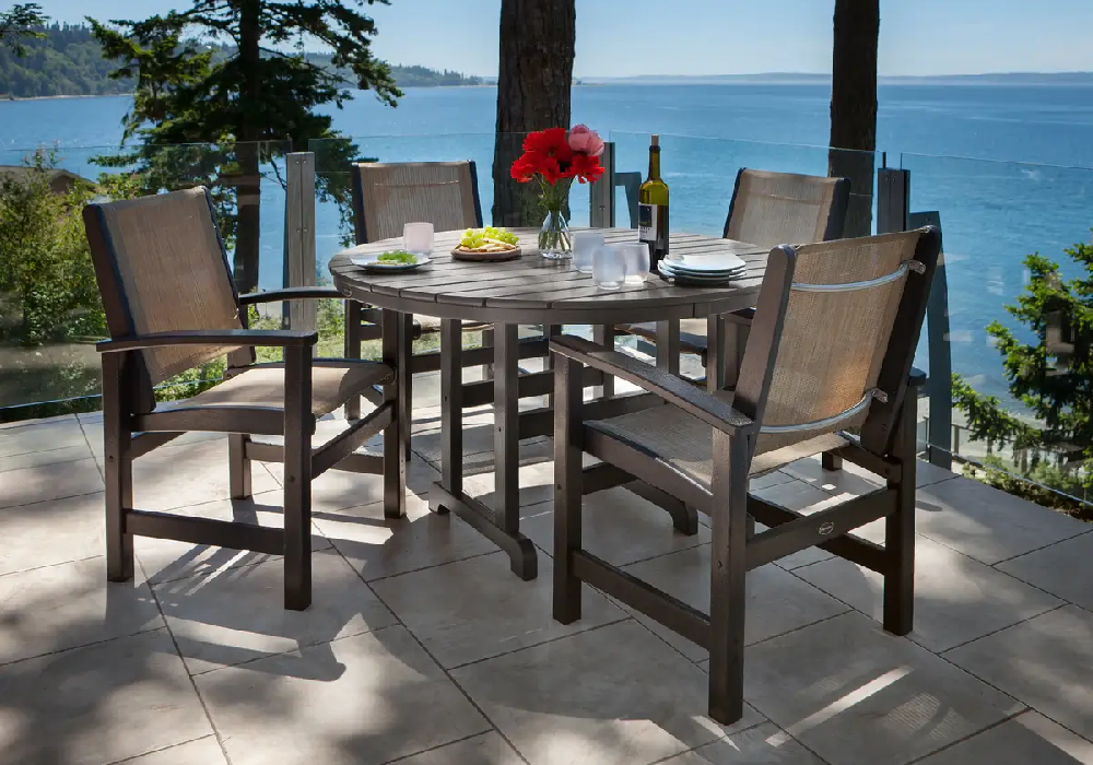 Outdoor dining set with sling chairs and a round table overlooking a waterfront view, ideal for resorts and luxury properties.
